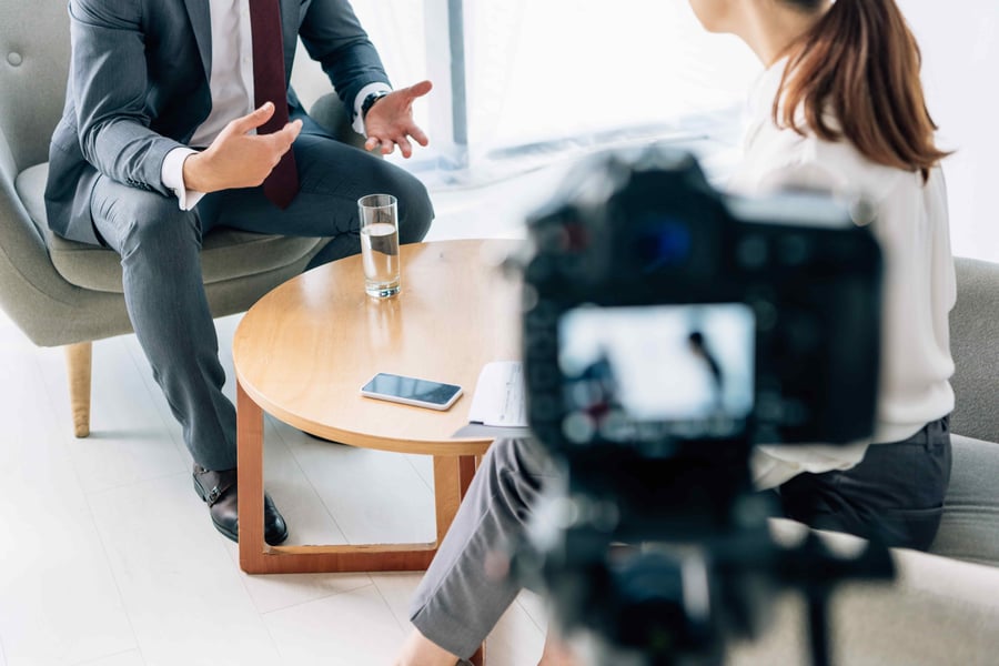 A business conversation captured on camera, focusing on a man in a suit gesturing with his hands during an interview. 