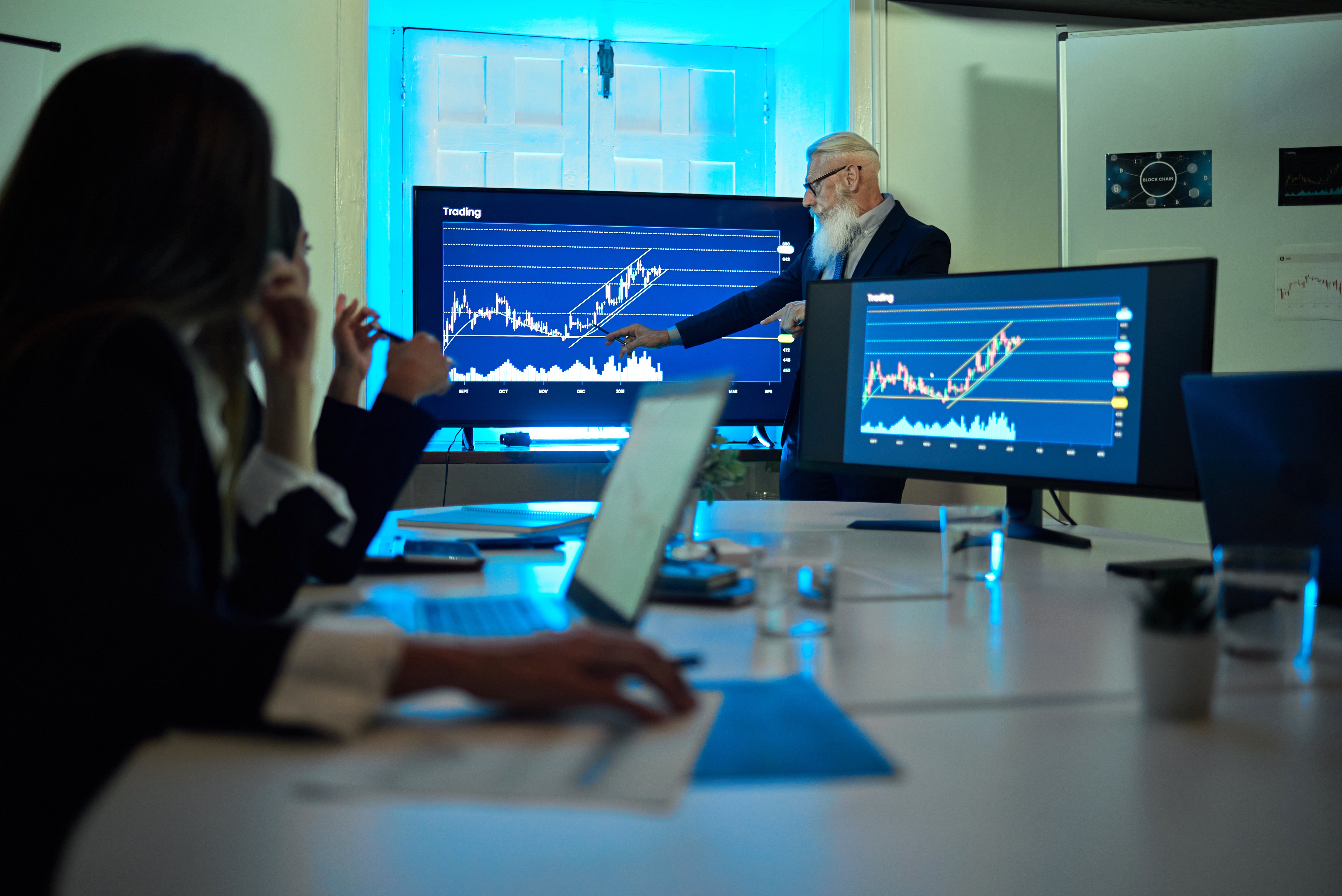 A business professional presents data trends on multiple screens during a meeting, highlighting growth strategies amid economic challenges