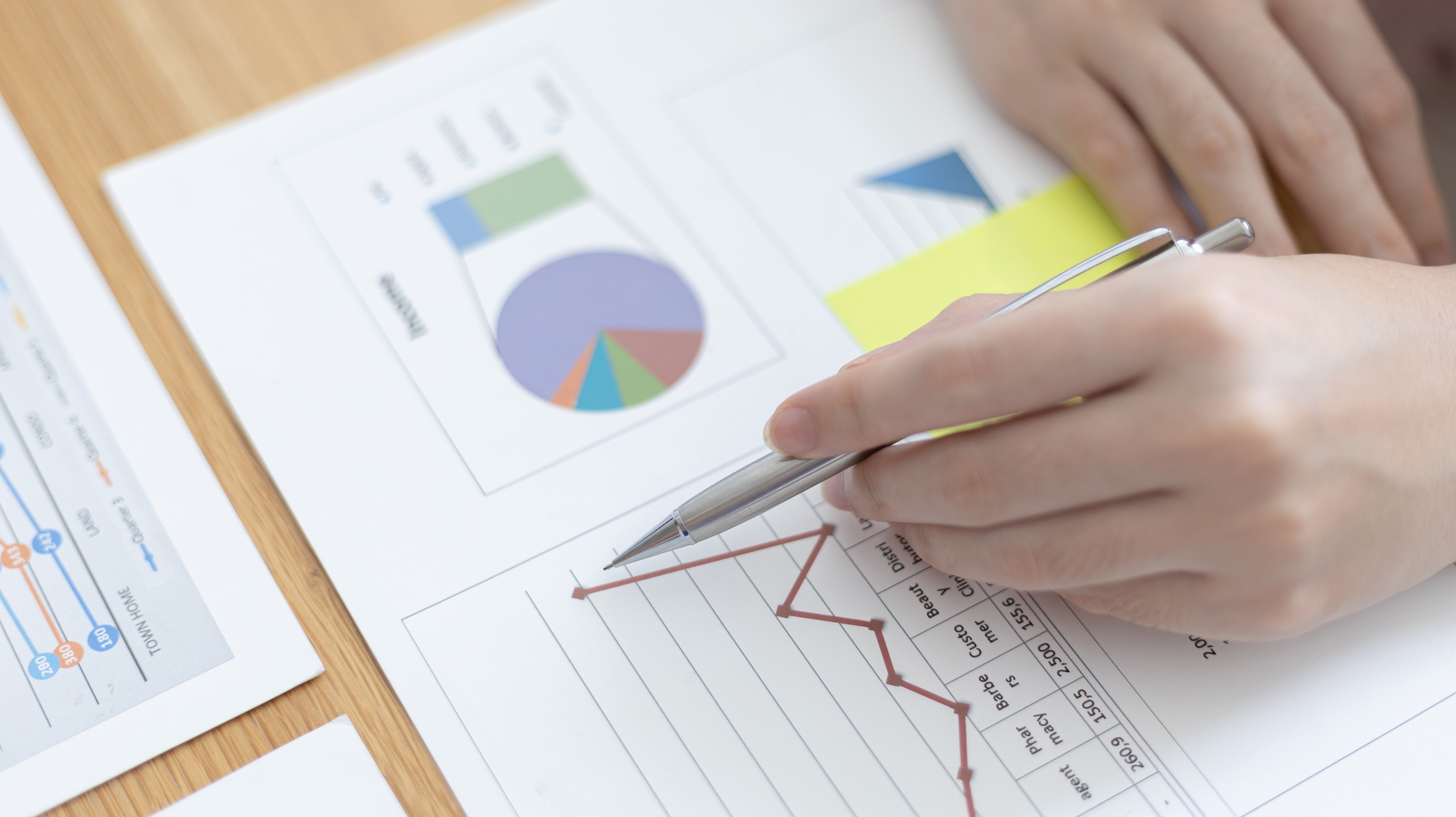 A close-up of a hand holding a pen while analyzing financial graphs and charts on paper.