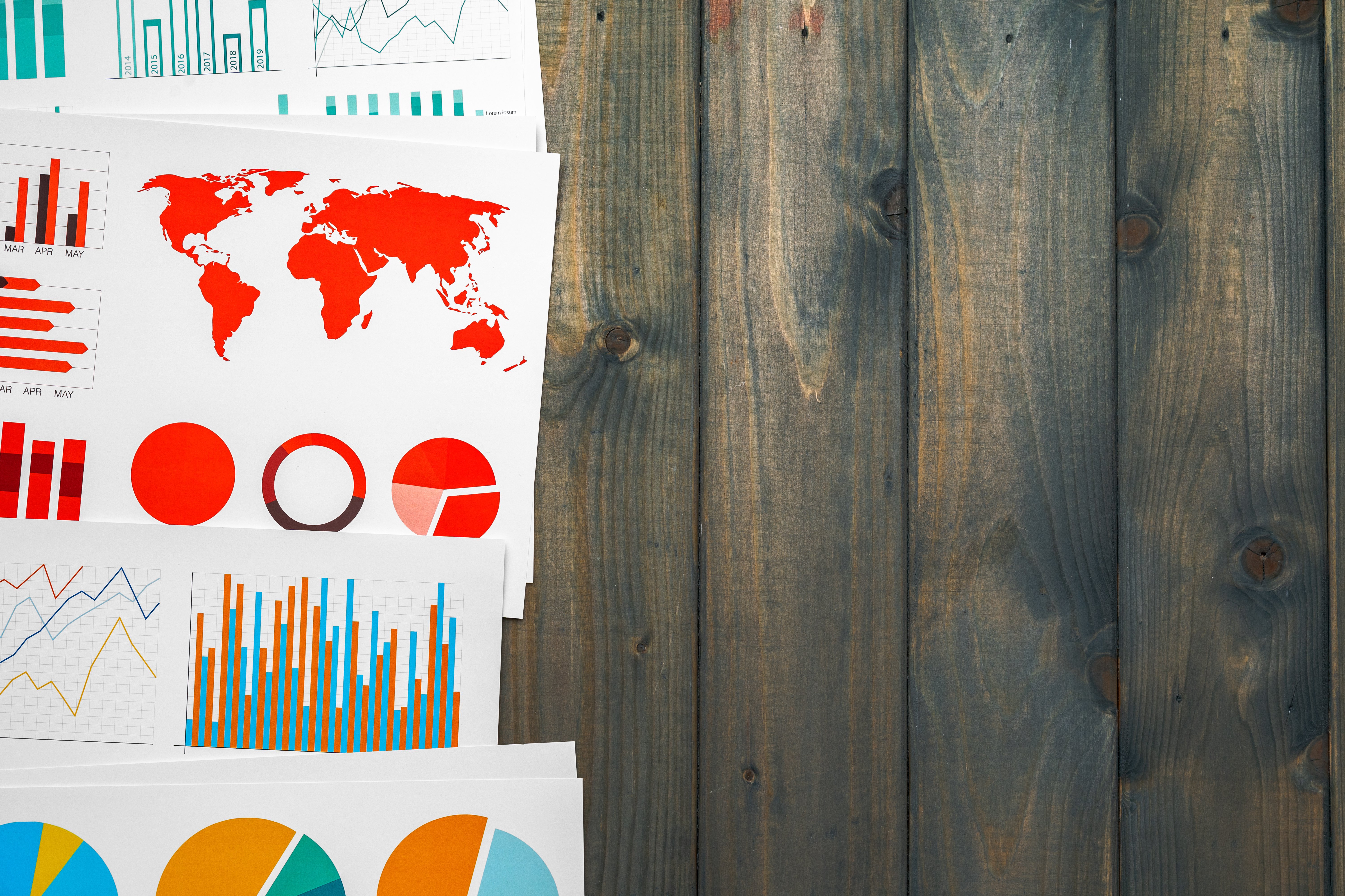 A collection of financial reports with charts and graphs, including a world map and pie charts, spread out on a wooden table.