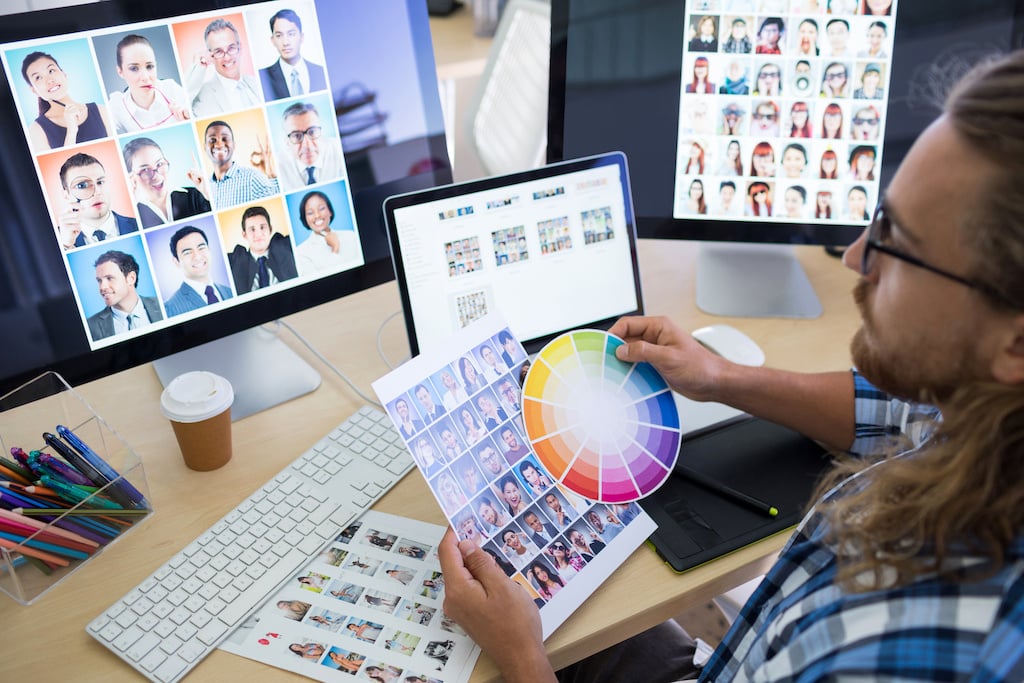 A designer reviews a colour wheel and selects images for a project on multiple monitors, focusing on diverse professional headshots