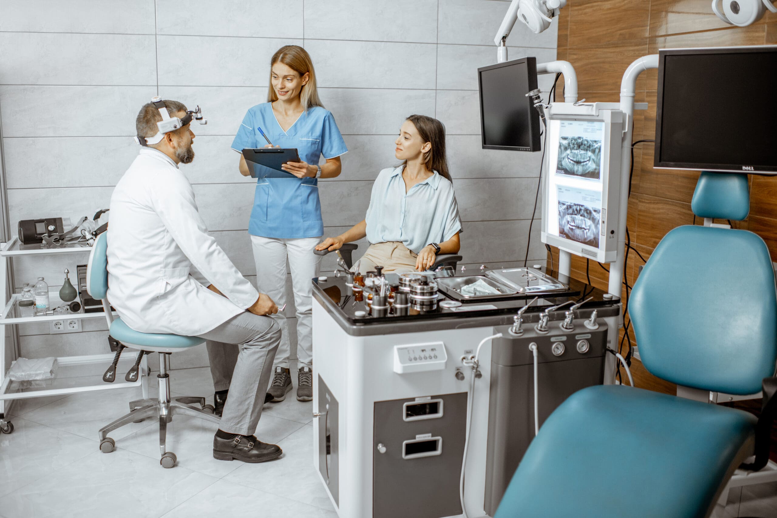 A doctor and nurse consult with a female patient in a modern ENT clinic, discussing her condition while viewing medical images on nearby screens.-min