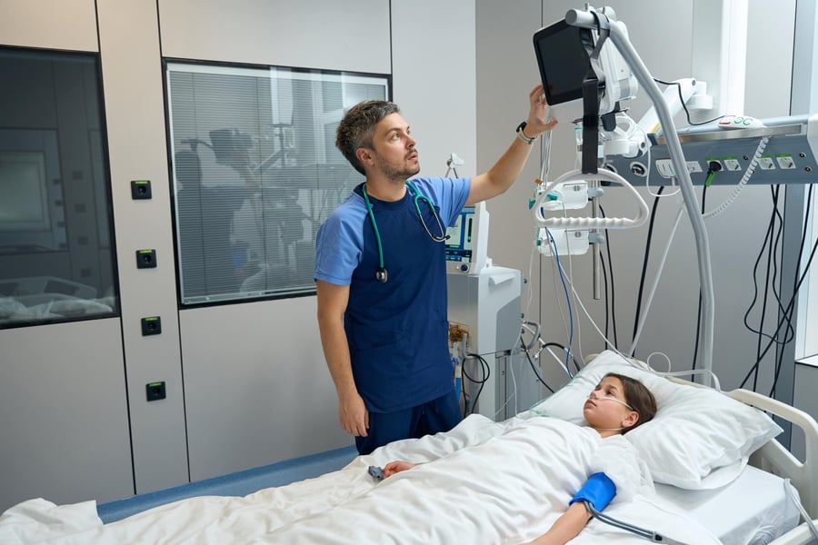 A doctor checking on his patient in a hospital room, surrounded by medical devices.
