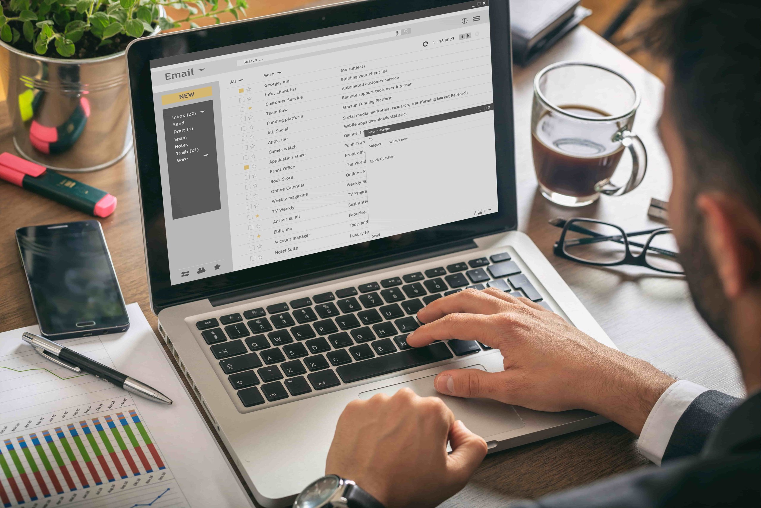 A person types on a laptop with analytical documents and a coffee cup on the wooden desk, focusing on work-related tasks with data sheets nearby.