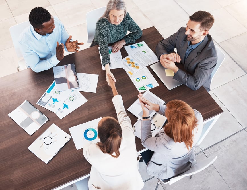 A top-down view of a diverse team collaborating on They Ask, You Answer content strategies for a medical device company, with charts and graphs spread across the table-