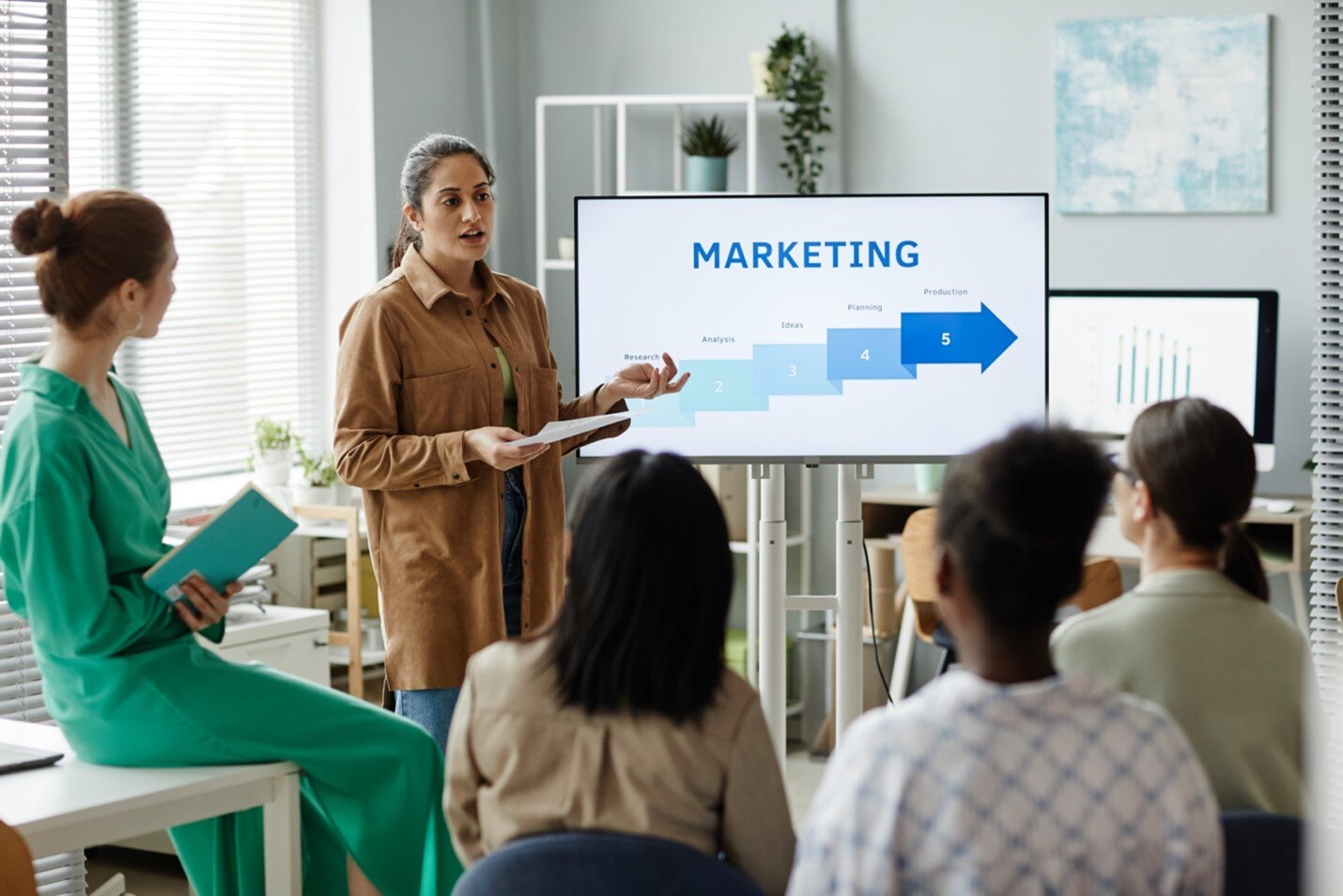 A woman presents a five-step marketing process to a small, attentive group in a modern office setting.