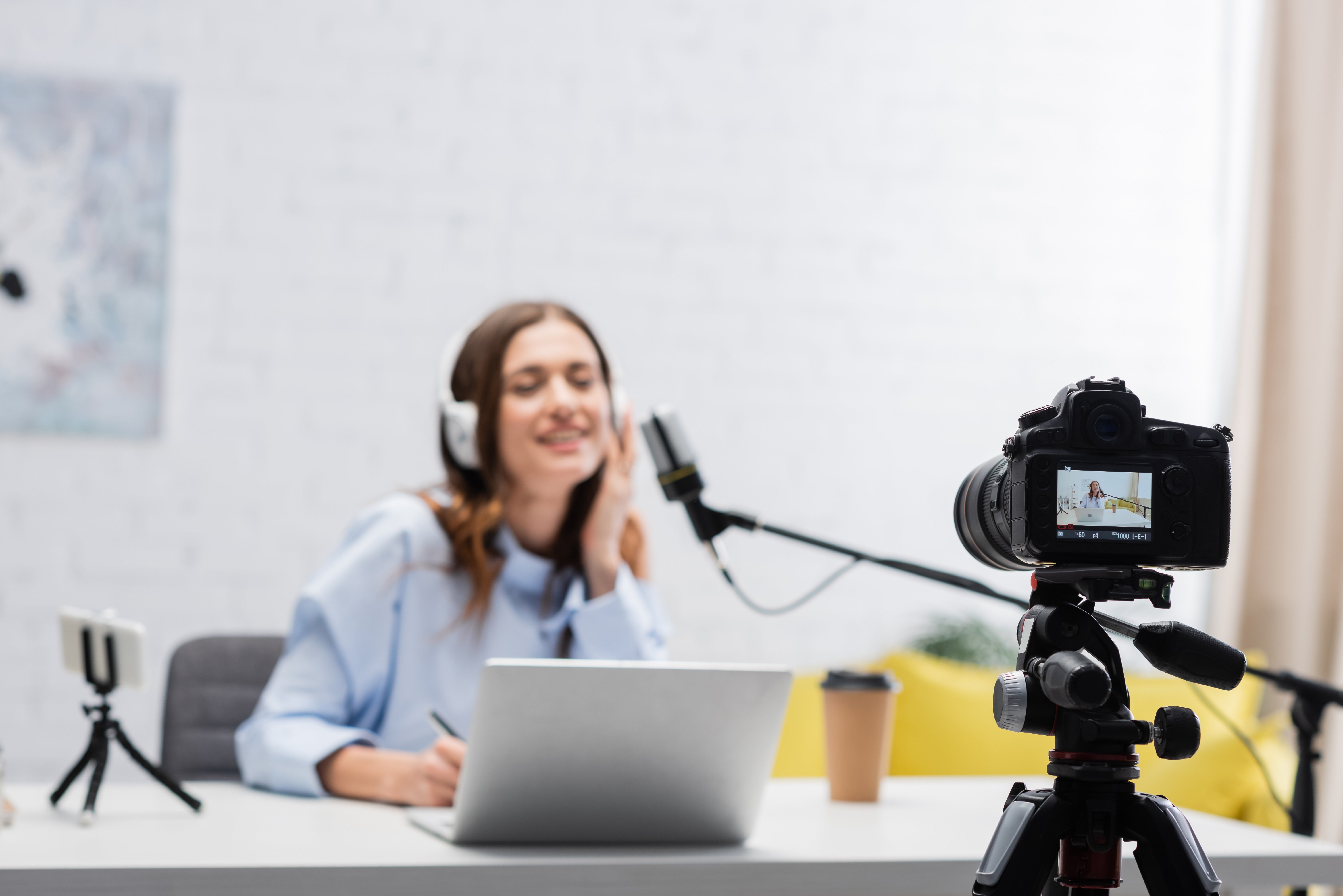 A woman wearing headphones smiles while recording herself with a camera in a professional studio setting.