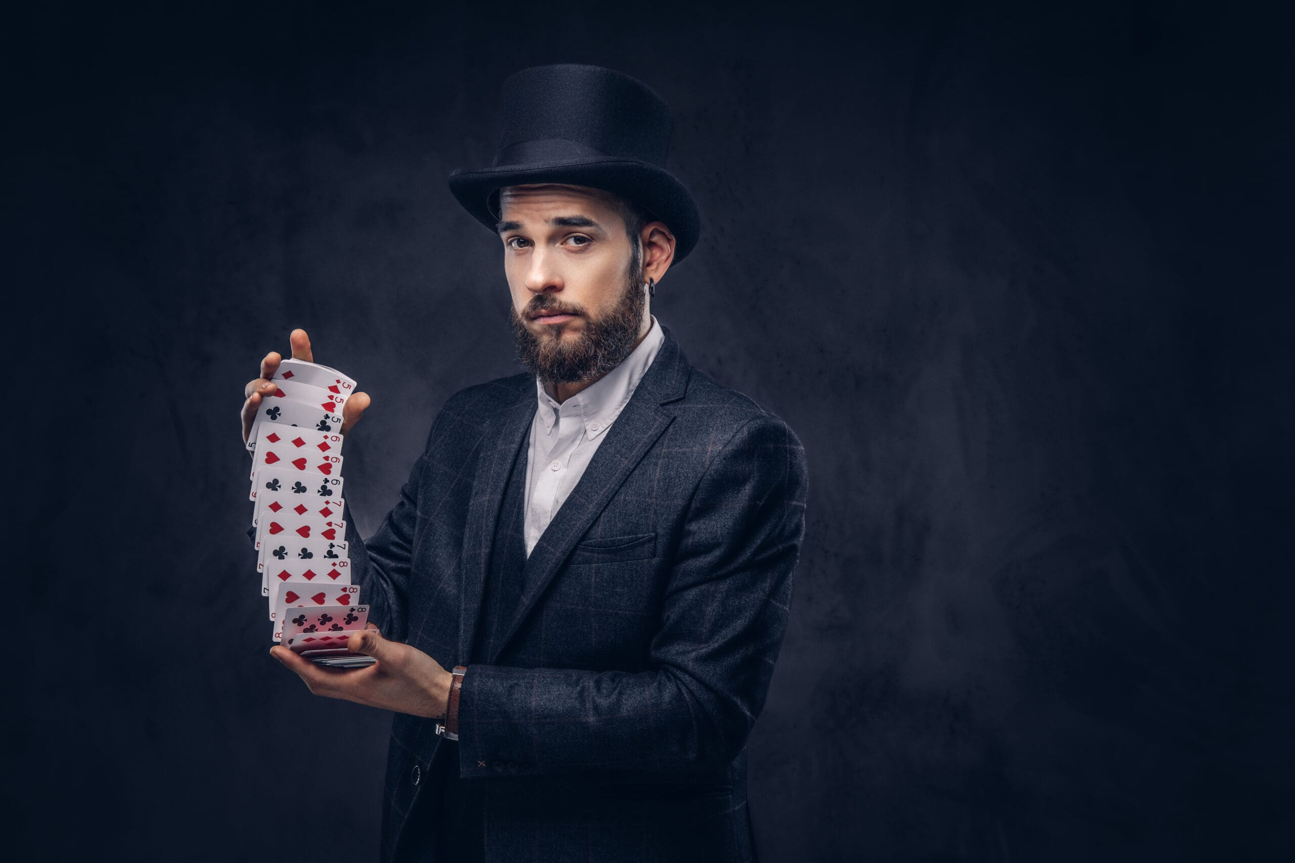 Bearded magician in a top hat performing a card trick, dressed in a dark suit.-min