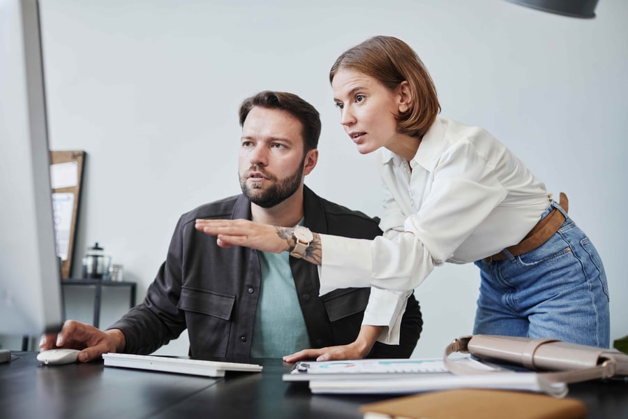 Two colleagues collaborate at a desk, with one pointing at images on a computer screen while the other observes closely. 