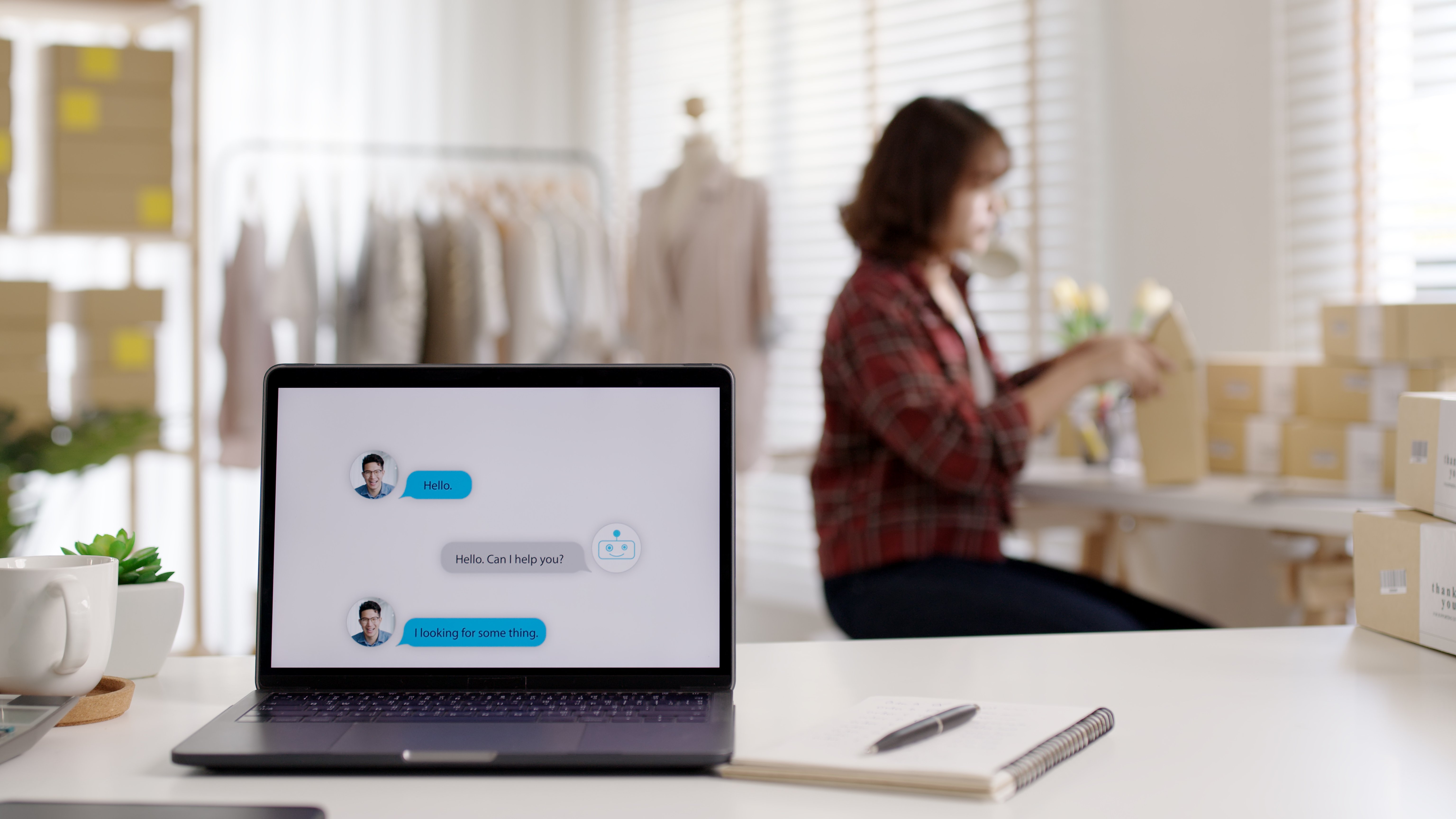 Business owner in a plaid shirt packs boxes in the background, while a chatbot conversation is displayed on a laptop in the foreground.