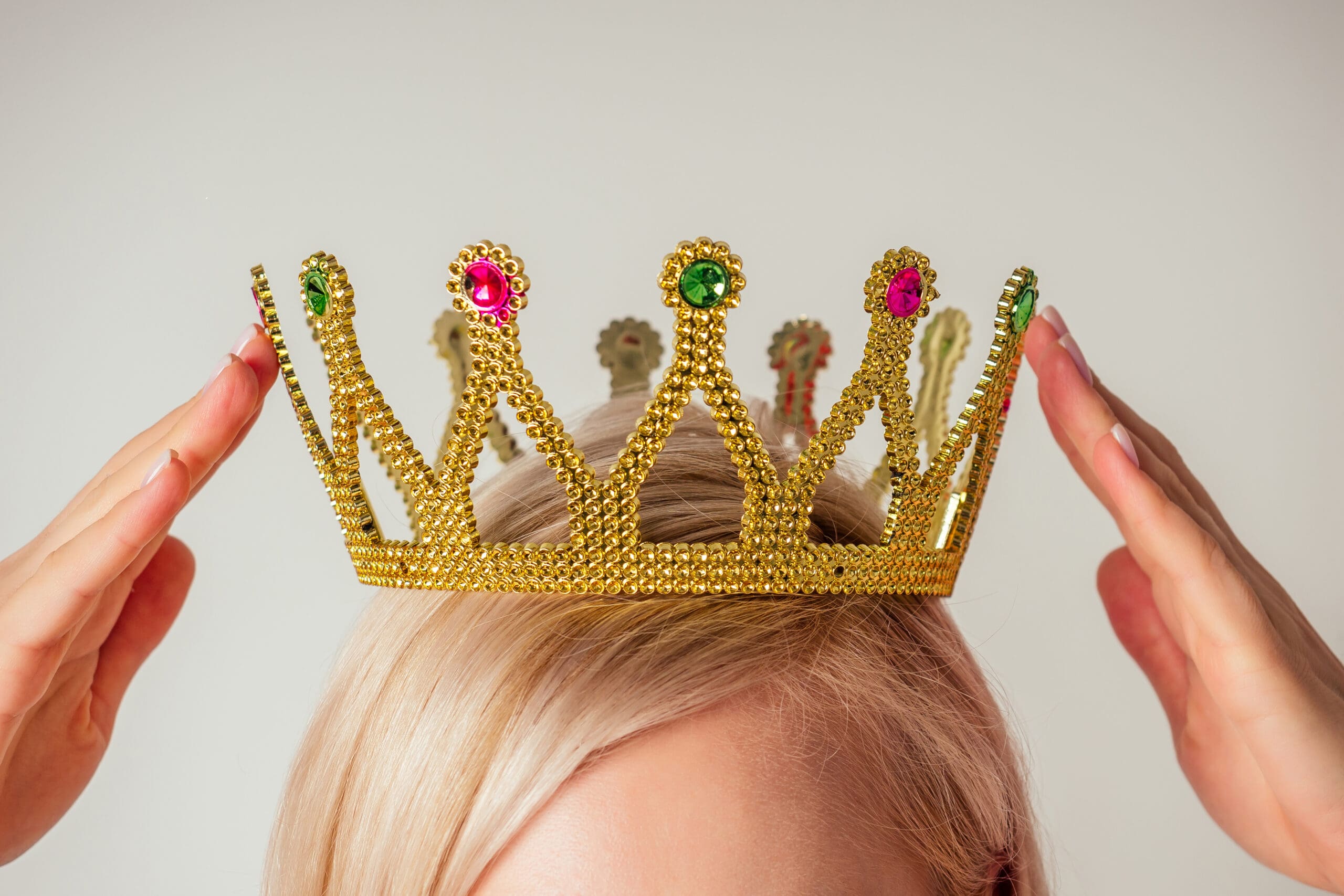 Close-up of a person placing a golden crown adorned with colourful gems on their head.-min