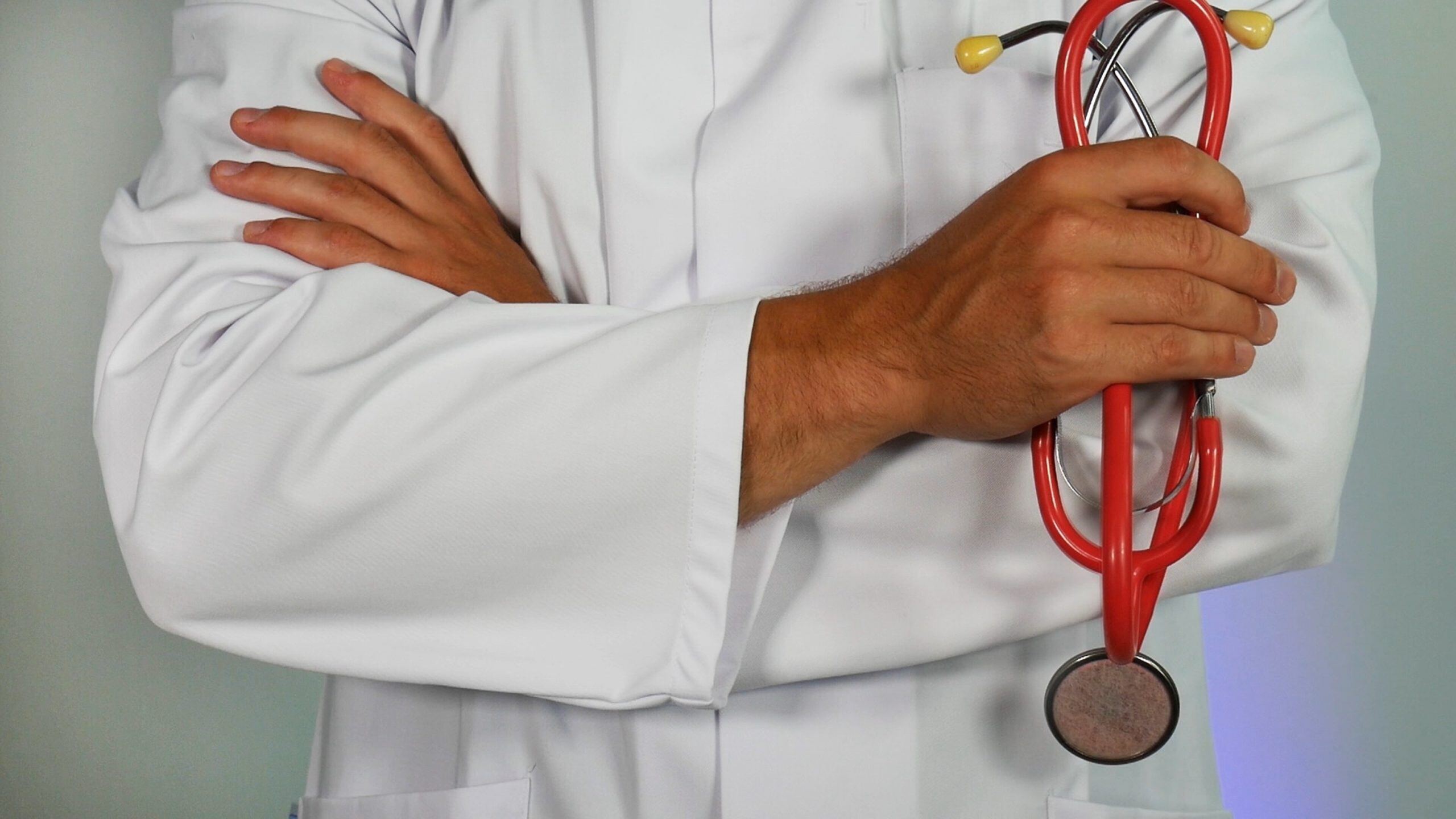 Doctor with arms crossed, holding a red stethoscope, symbolising professionalism and healthcare expertise.