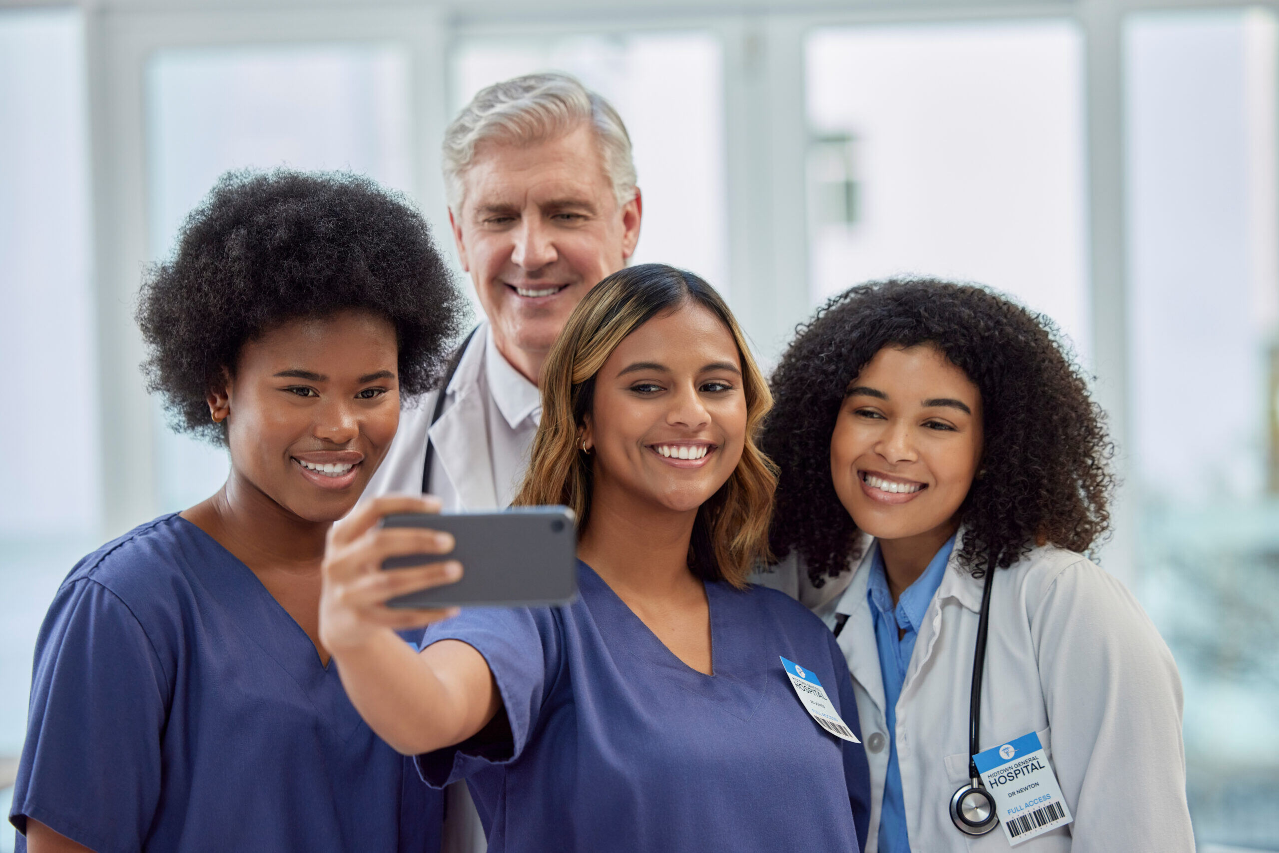 Four healthcare professionals, including two nurses and a doctor, smile for a selfie together, showcasing teamwork and camaraderie in a hospital setting.