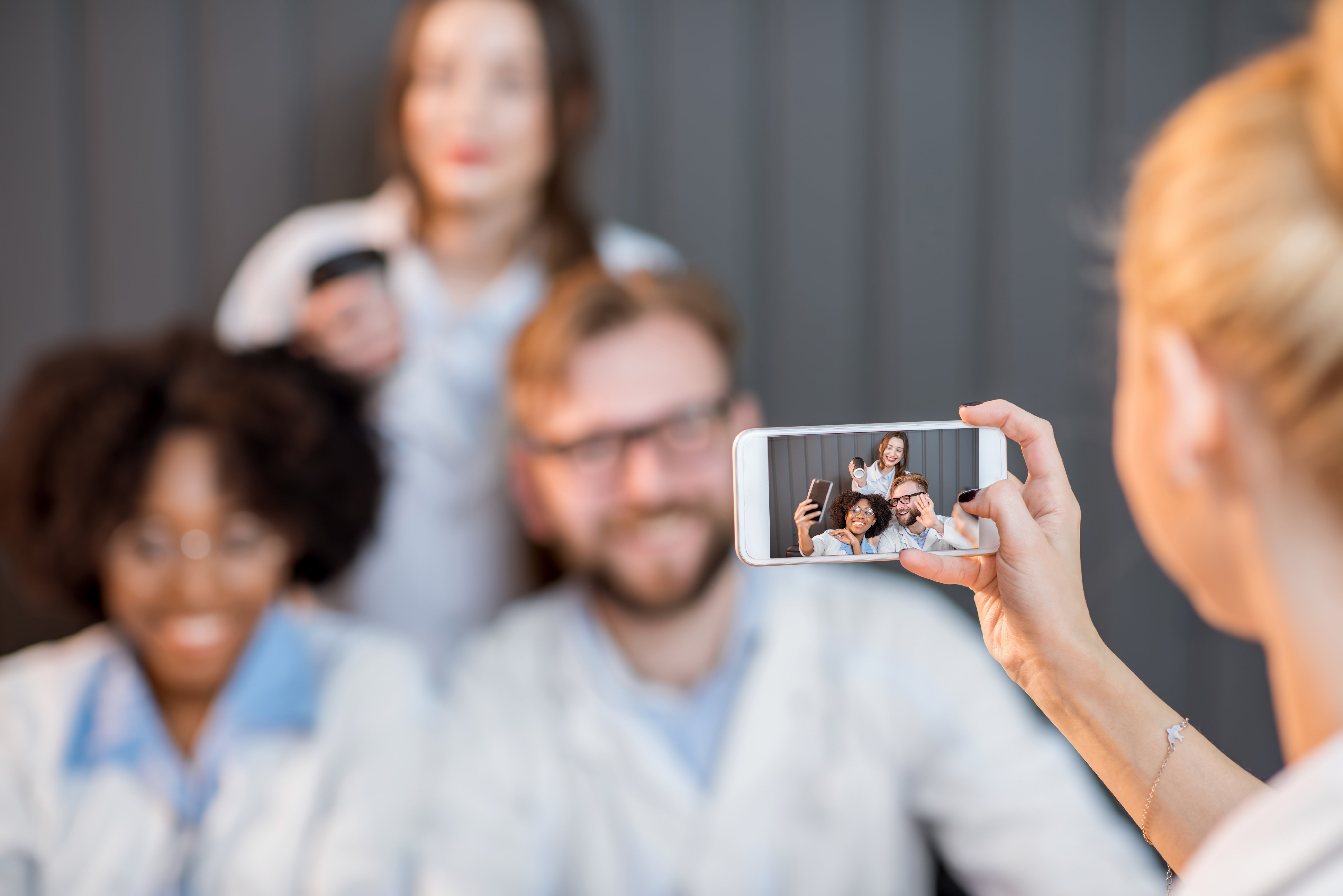 Four medical professionals in lab coats taking a cheerful group selfie with a smartphone