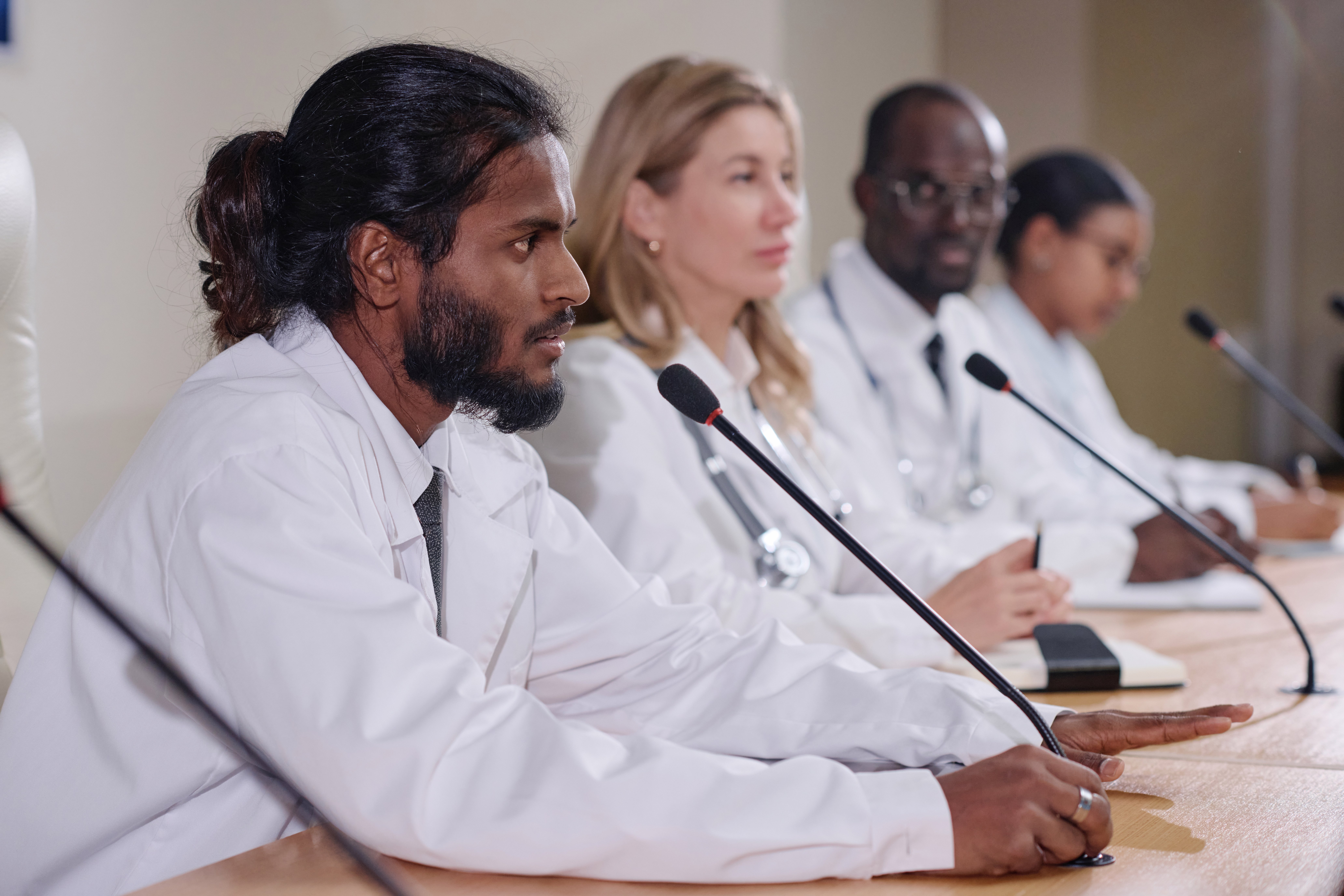 Healthcare professionals on a conference panel in white lab coats, with a focus on the front speaker addressing the audience