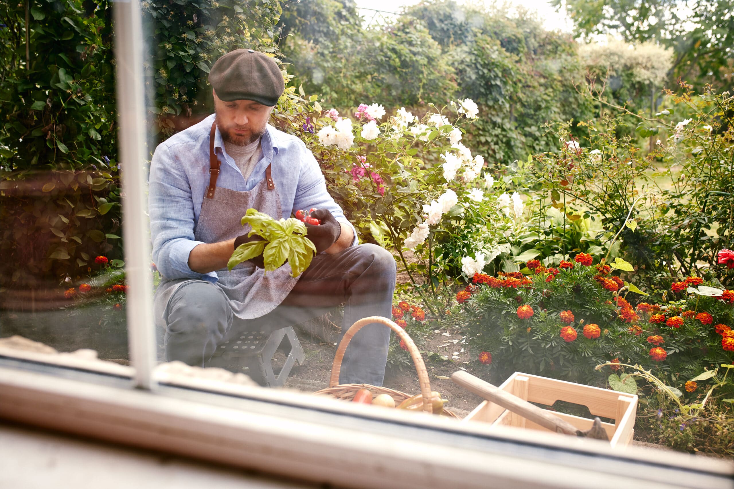 Male farmer in an apron holding fresh vegetables while sitting in a vibrant garden.-min