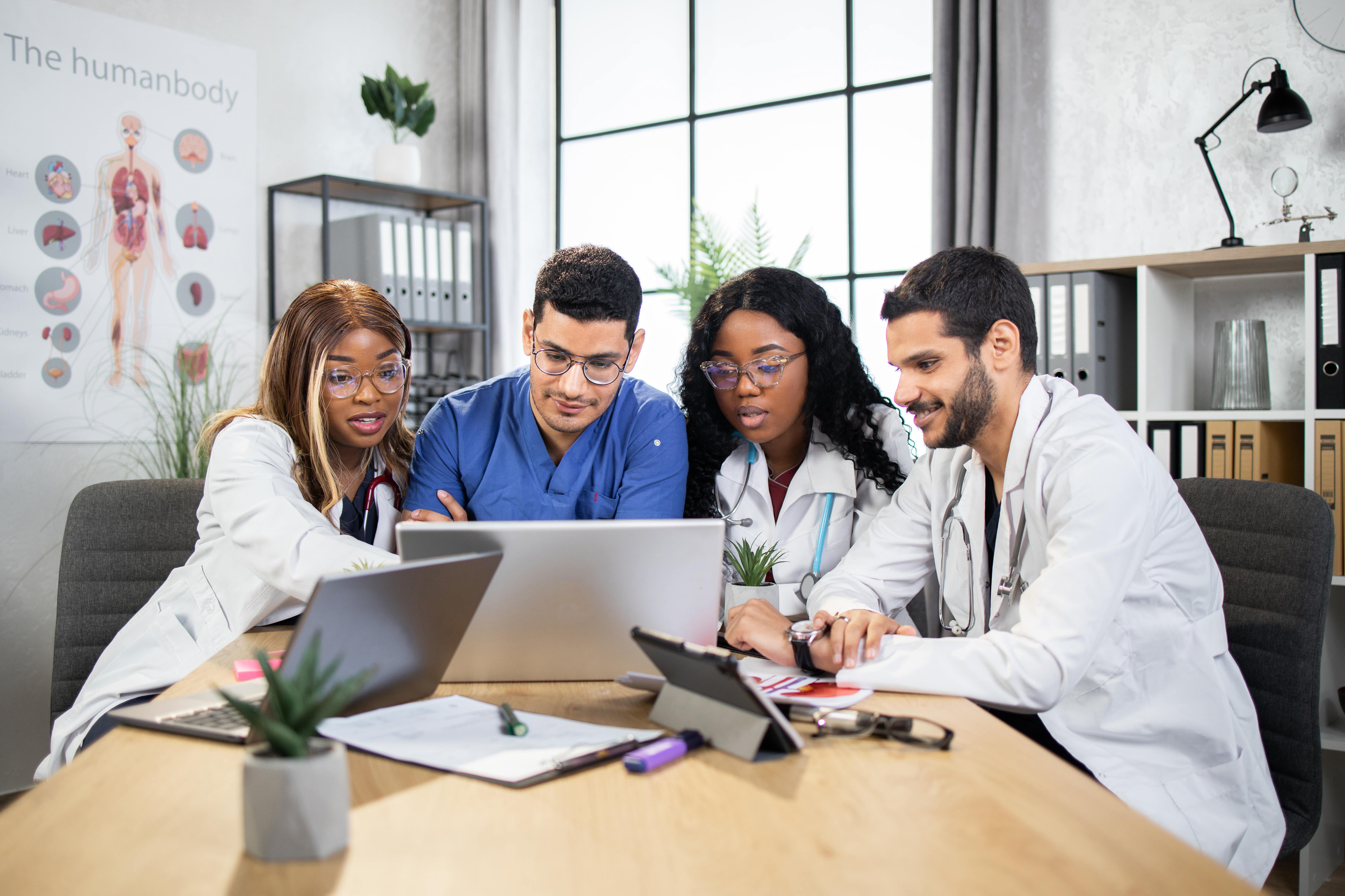 4 healthcare professionals gathered around a laptop, viewing a medical device webinar.