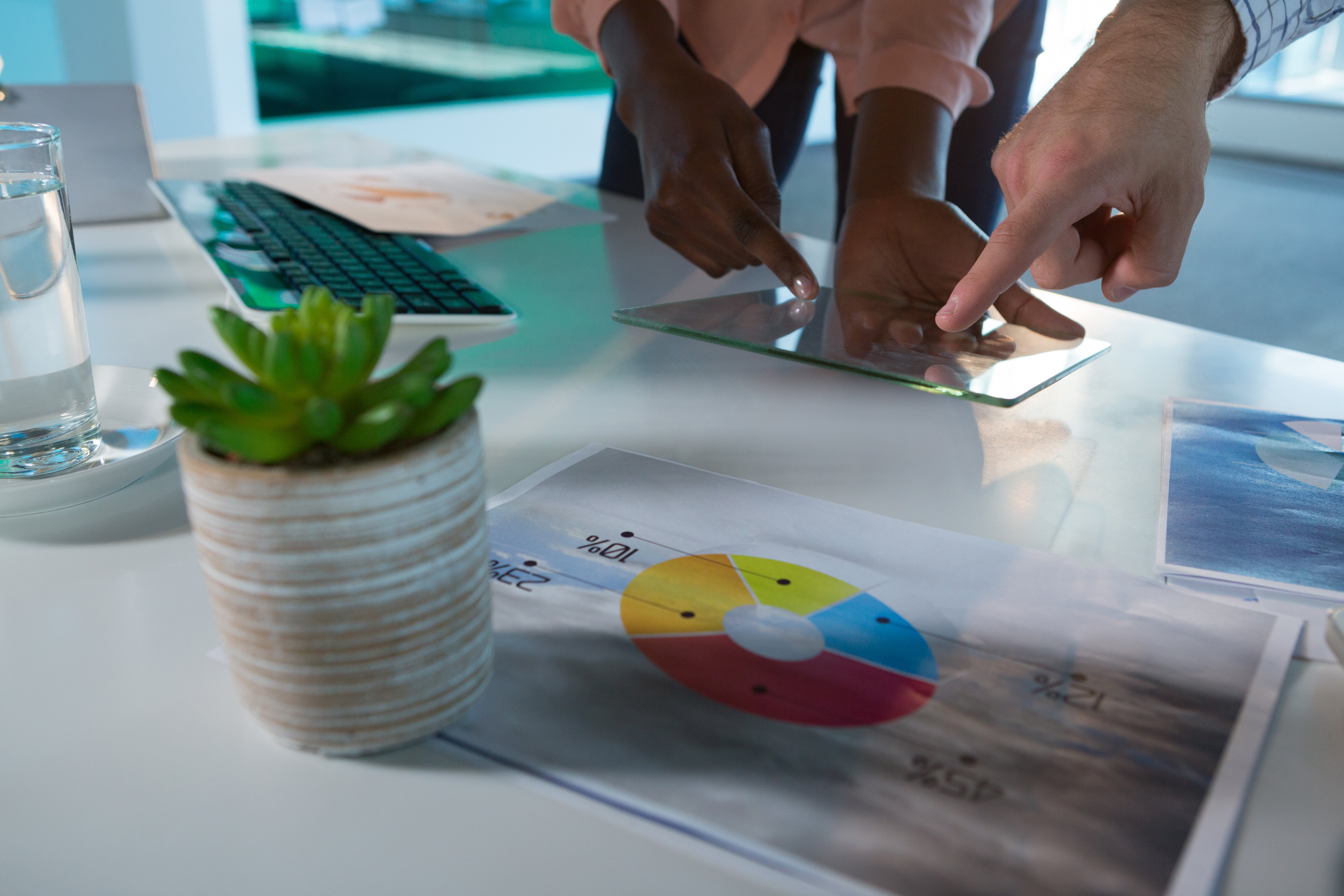 Two business professionals review pie charts and data on a tablet, discussing financial reports at a modern office desk