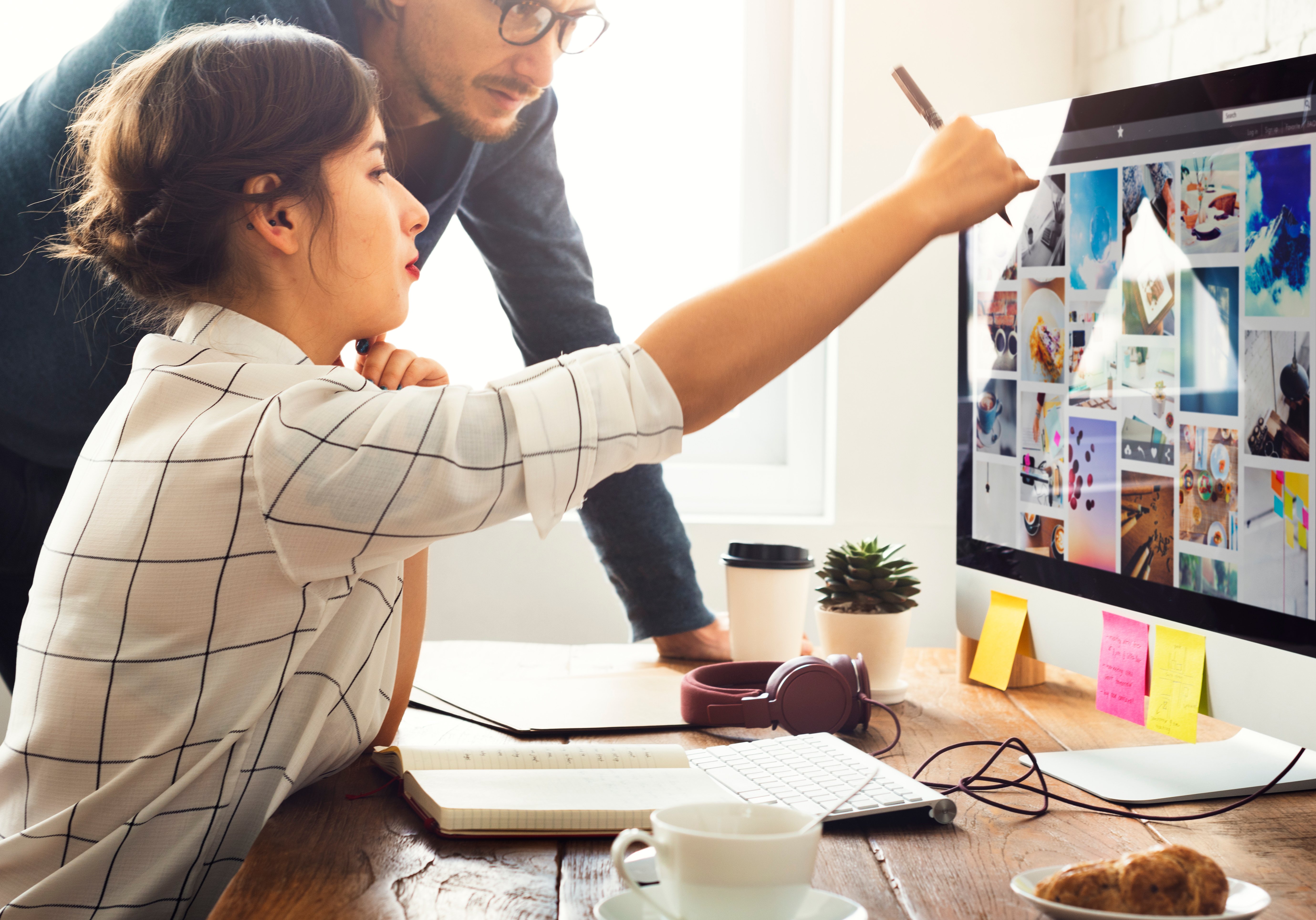 Two colleagues collaborate at a desk, with one pointing at images on a computer screen while the other observes closely.