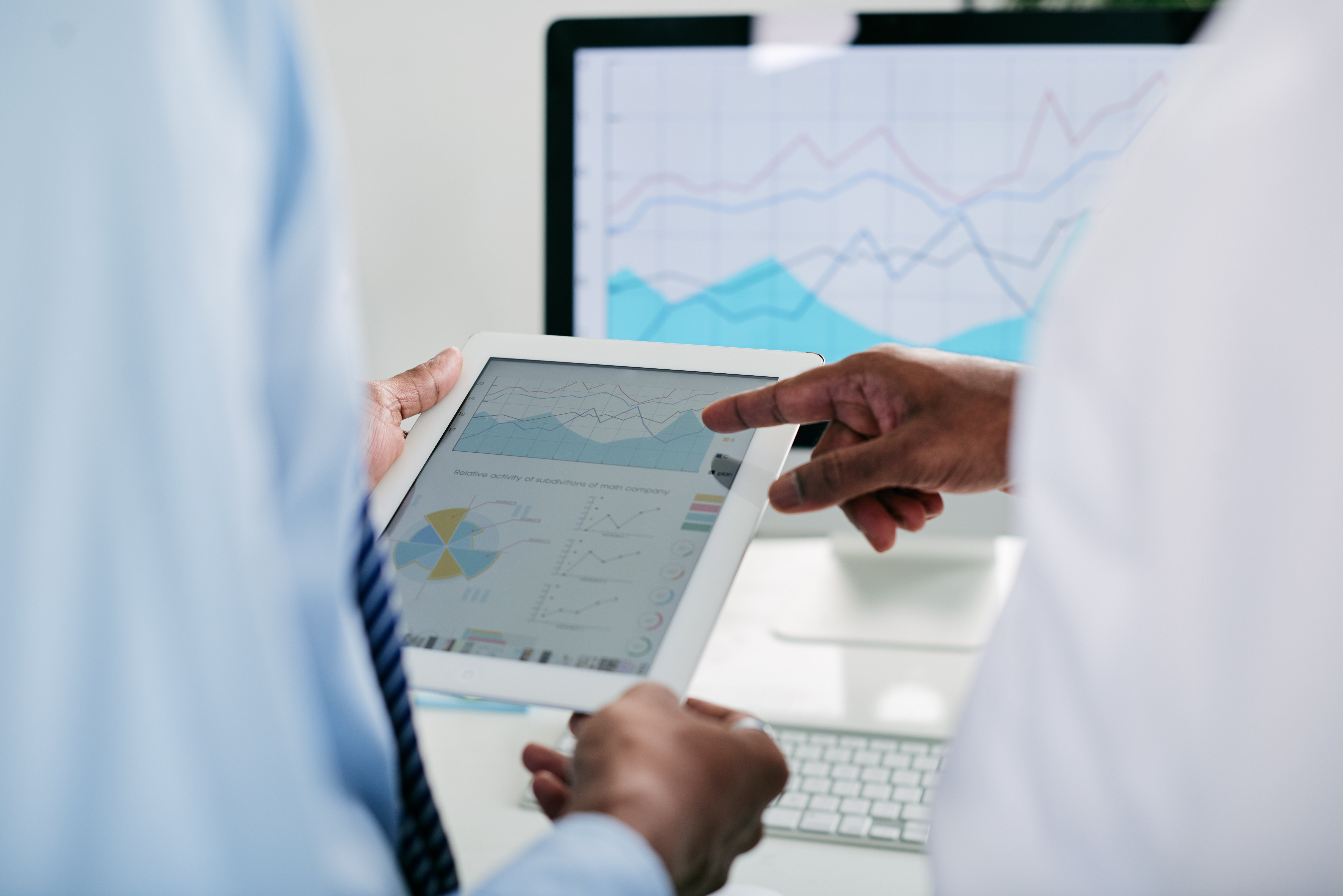 Two professionals discussing data on a tablet with graphs and charts in a modern office setting.-1