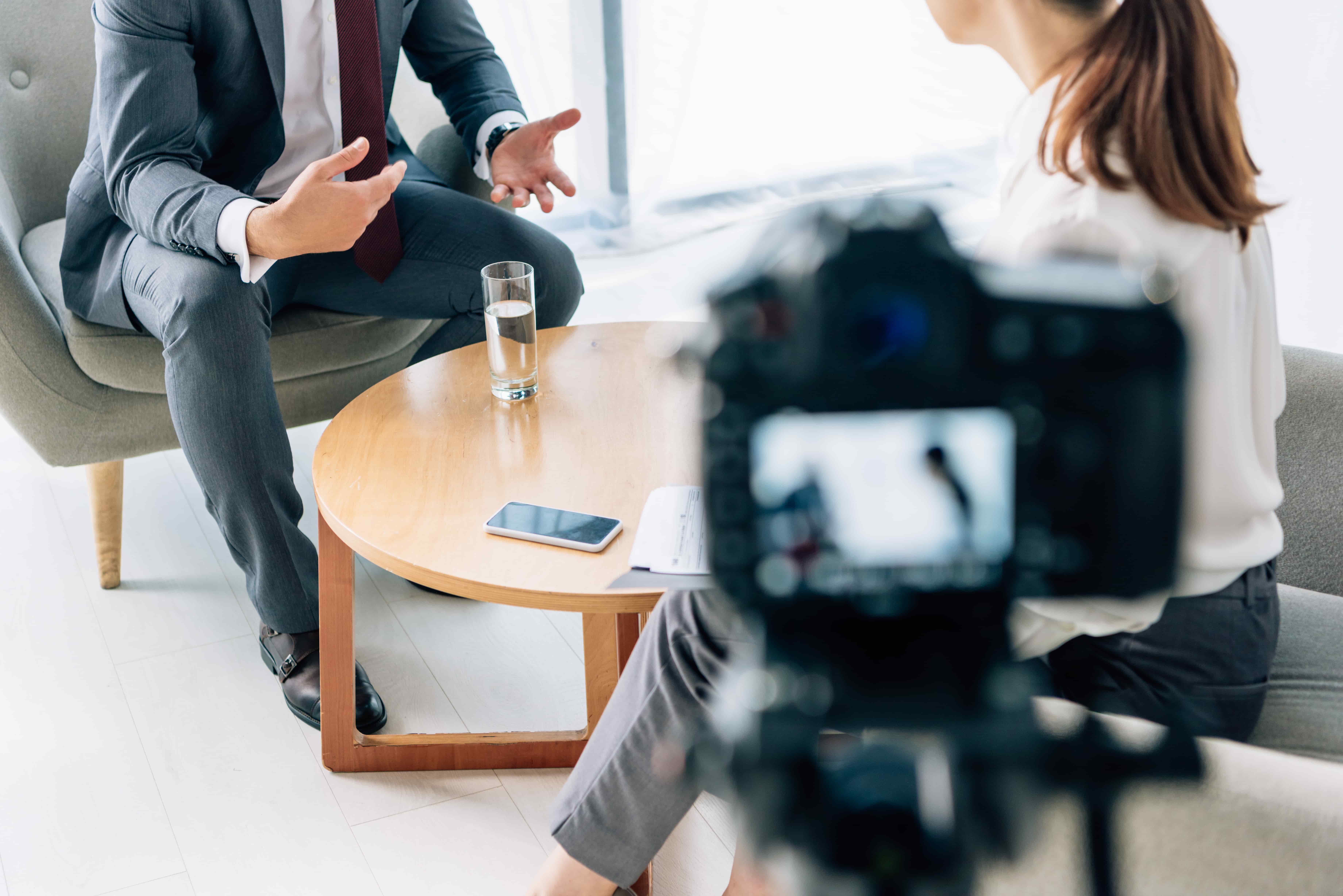 A business conversation captured on camera, focusing on a man in a suit gesturing with his hands during an interview. 