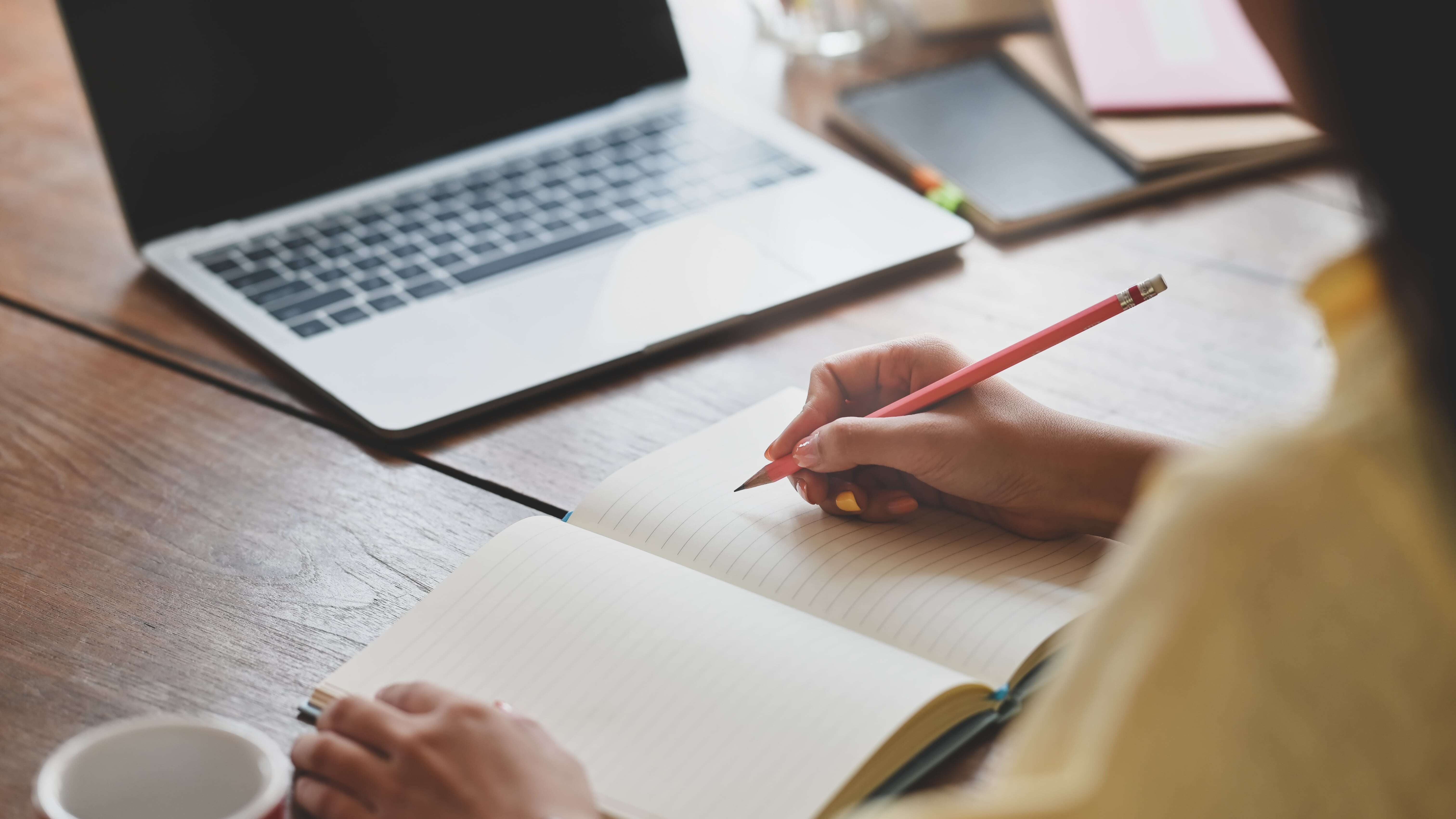 A medical device marketer works on their content writing skills on a wooden desk in a notebook.