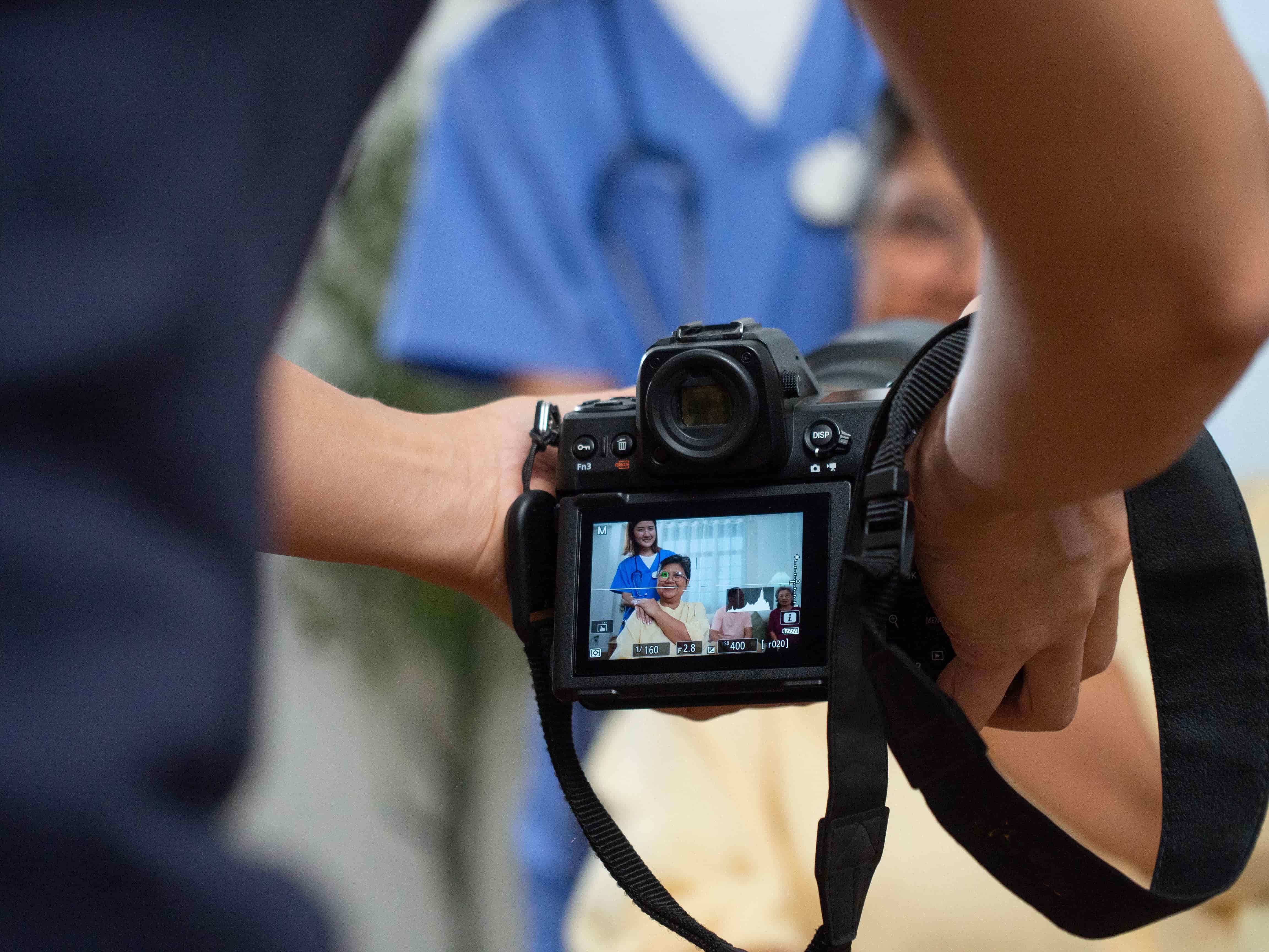 Photographer capturing a video interview with a healthcare professional, as seen through the camera's display screen, with the subject smiling and engaging with the camera.