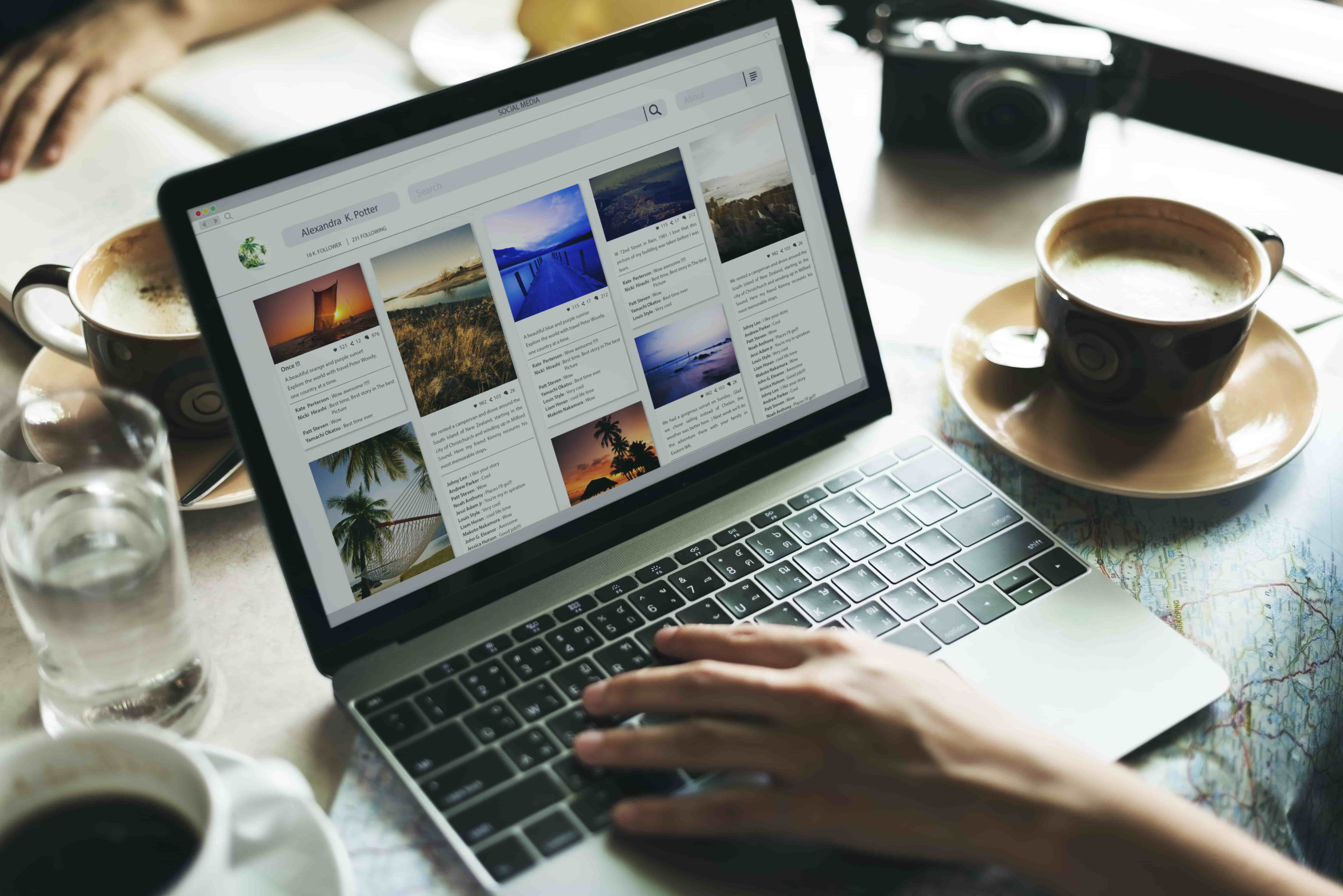 A laptop displaying a social media page with photo posts. Surrounding the laptop are cups of coffee, a map, and a camera. 